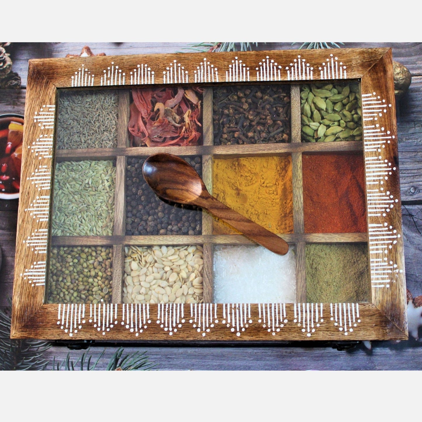 Handcrafted and Hand Painted Mango Wood Spice box with 12 large partitions and glass top. Showing the top view with free wooden spoon.