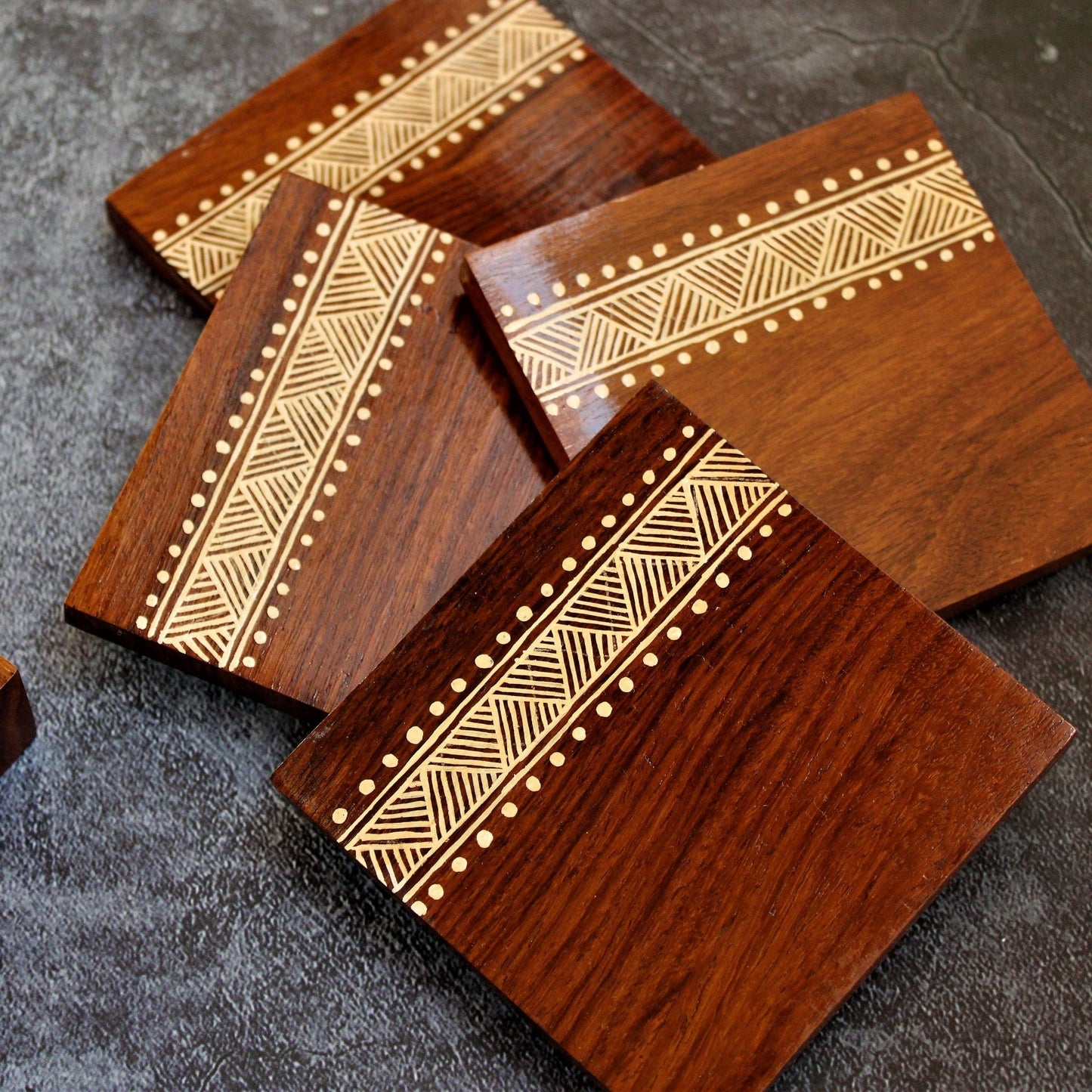 Indian Rosewood Hand Painted and Well Finished Coaster Set with Stand. It is a set of four coasters with hand painted aipan inspired design on them.