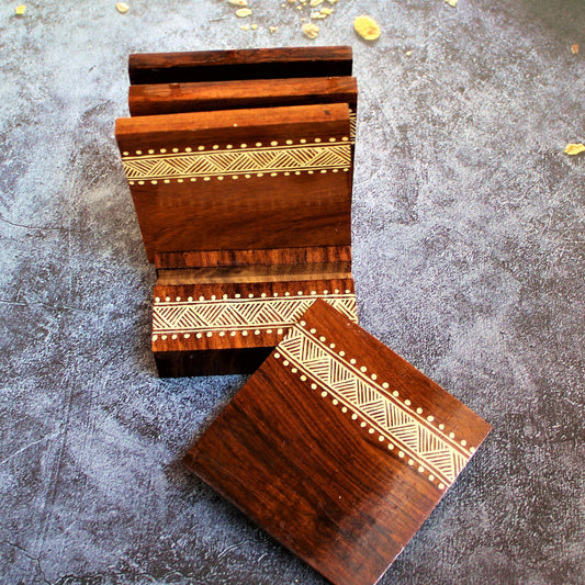 Indian Rosewood Hand Painted and Well Finished Coaster Set with Stand. It is a set of four coasters with hand painted aipan inspired design on them.