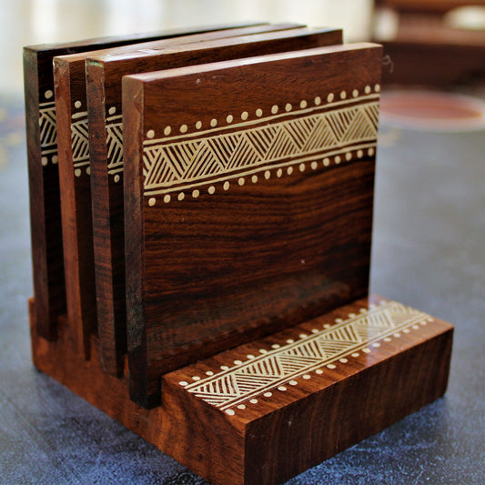 Indian Rosewood Hand Painted and Well Finished Coaster Set with Stand. It is a set of four coasters with hand painted aipan inspired design on them.
