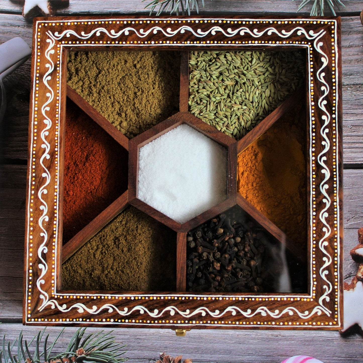 Aipan Inspired Hand Painted and Handcrafted Wooden Spice Storage Box with Glass Top and Free Wooden Spoon. Showcase Your Spices and other condiments with style. Alternatively Store Tea Bags, Dry Fruits and other condiments of the kitchen. In this box one can store up to seven different spices /teas / condiments. It is beautifully hand painted by women folk of Uttarakhand to give it the traditional look.